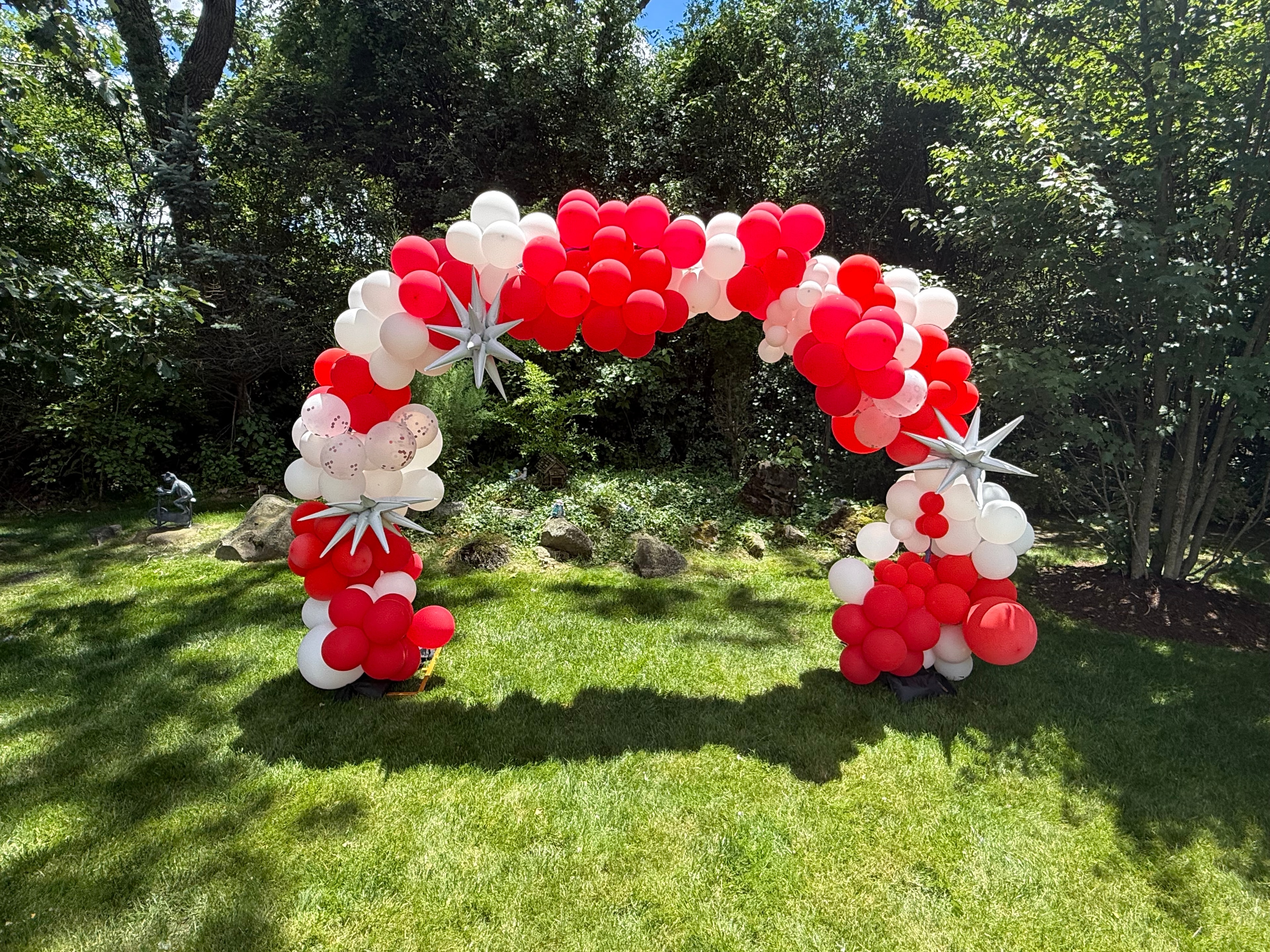 Large red, white, and silver star balloon arch built in a backyard by Violette — custom graduation party styling, Chicago suburbs
