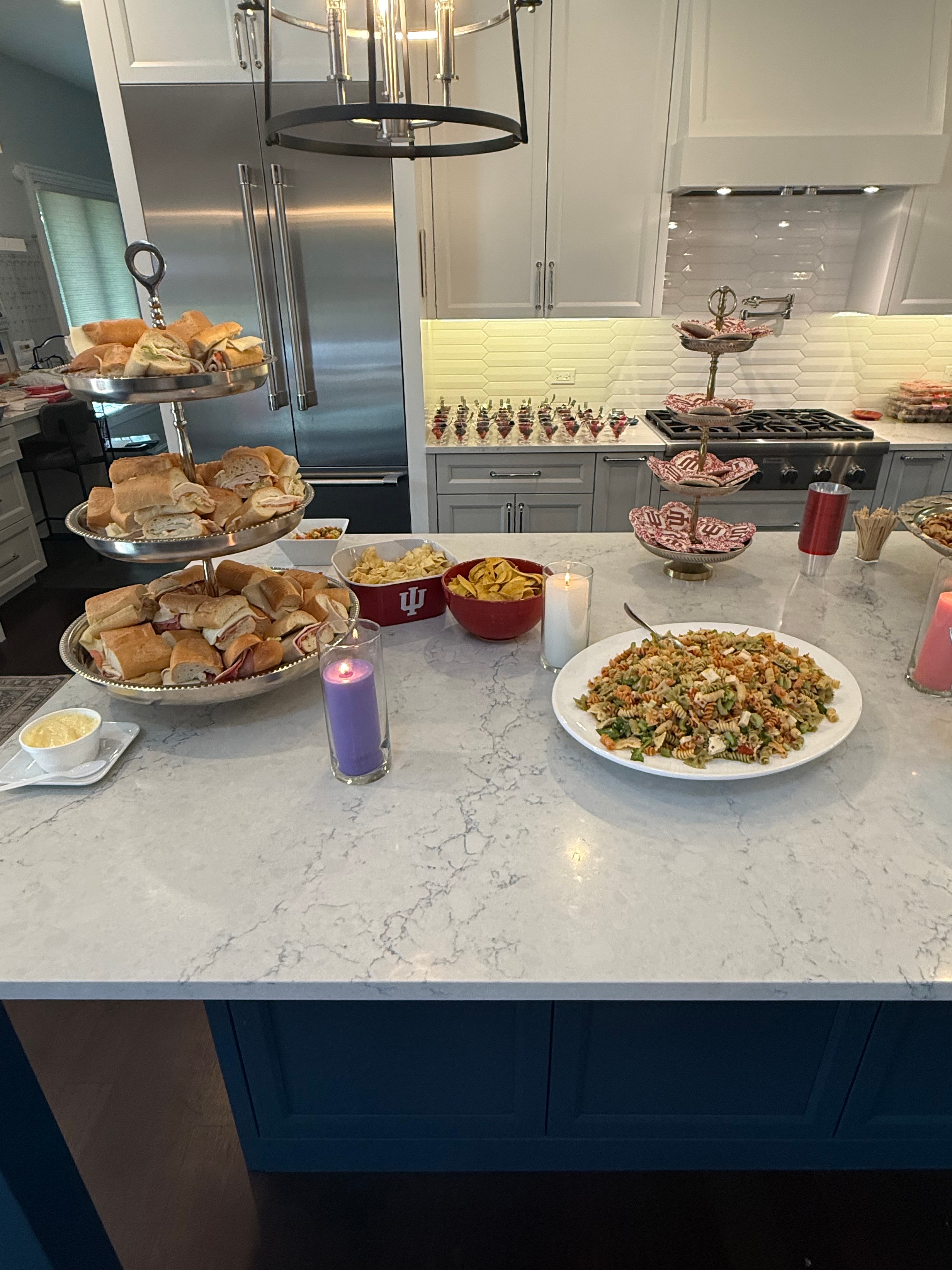 Full kitchen island spread with sub sandwiches, pasta salad, themed snacks, and candles styled by Violette for a private graduation celebration — Chicago suburbs